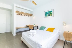 Habitación de hotel con cama, escritorio, silla, ventilador de techo y un cuadro en la pared.