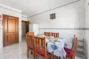 Ein Essbereich mit einem Tisch für vier Personen, Stühlen, einem Kühlschrank und einer gefliesten Spritzschutzwand.