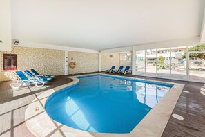 An indoor swimming pool with blue water, surrounded by lounge chairs and a stone wall. - Luxury Apartment Pool EV Charger (Portimão)