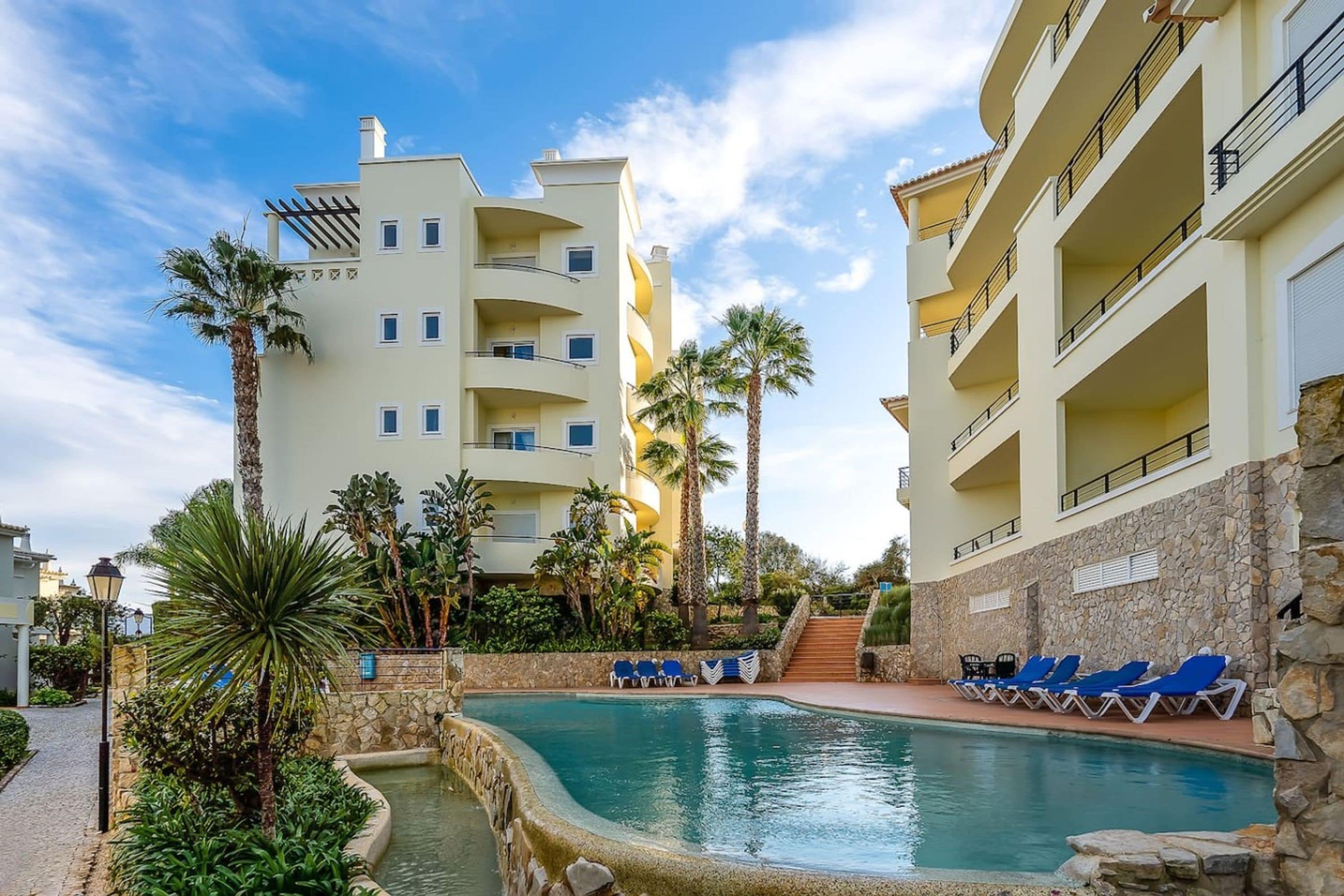 A hotel with a swimming pool surrounded by palm trees and lounge chairs.