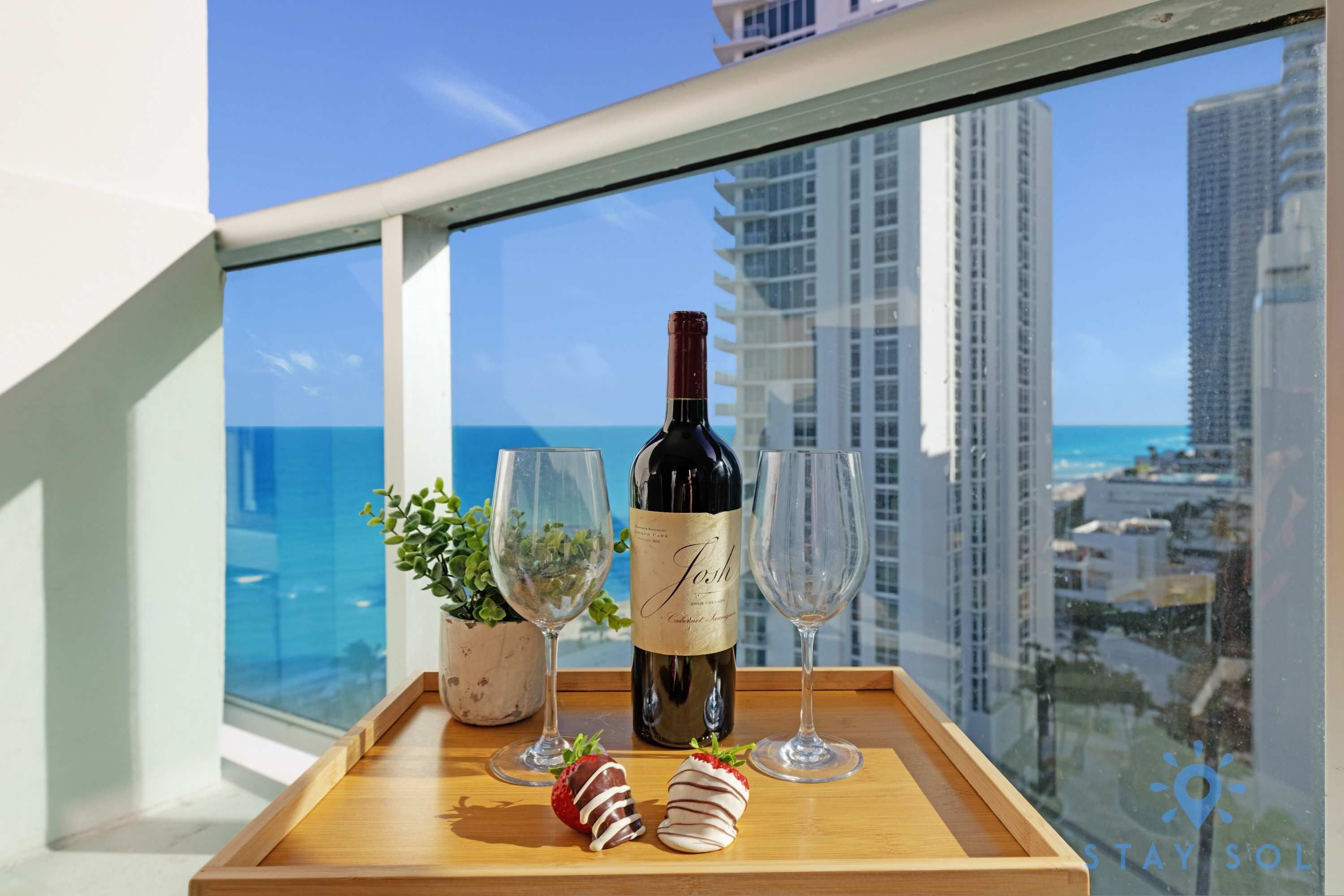 Un balcon avec une bouteille de vin, deux verres et des fraises disposées sur un plateau.