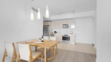 A modern kitchen with stainless steel appliances, a dining area with a wooden table and chairs, and pendant lighting.