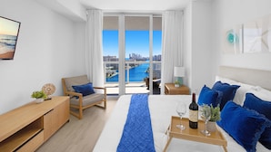 Ein modernes Hotelzimmer mit einem großen Bett, einem Schreibtisch, einem Stuhl und Blick auf Stadt und Meer vom Balkon aus.