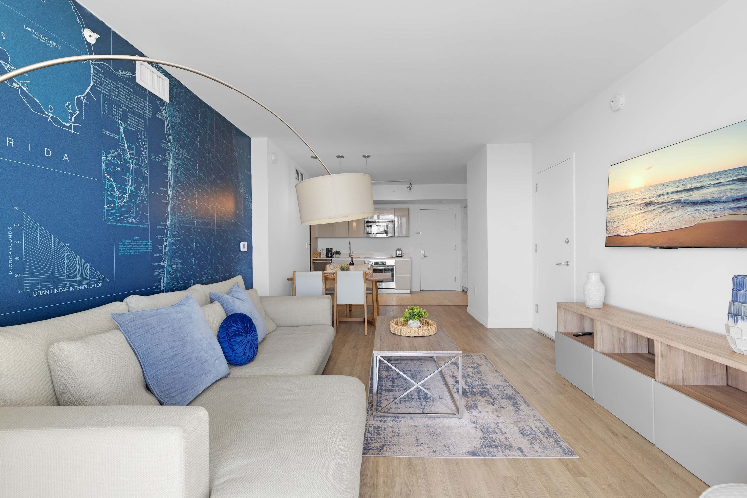 A modern living room with a large map on the wall, a sofa, a coffee table, and a kitchen in the background.