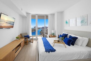 A modern hotel room with a large bed, a desk, a chair, and a view of the city and water.