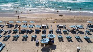 Een strand met rijen ligbedden en parasols, een zandstrand en de oceaan op de achtergrond.