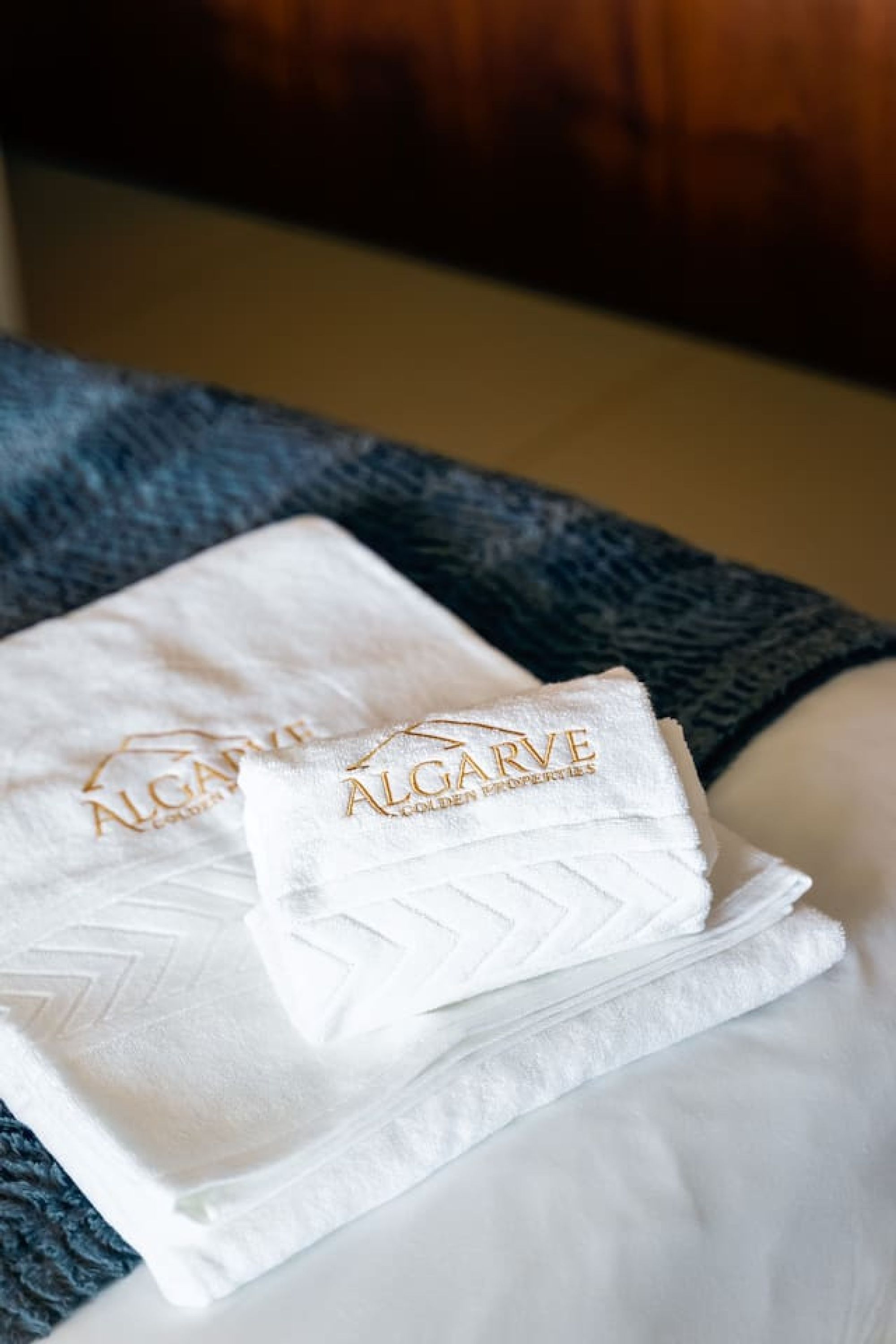 Two white towels with gold embroidery on a bed.