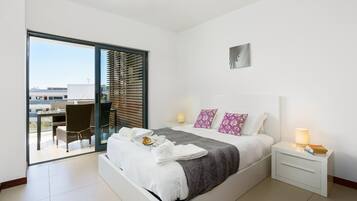 A modern hotel room with a large bed, a balcony with a dining area, and a city view.