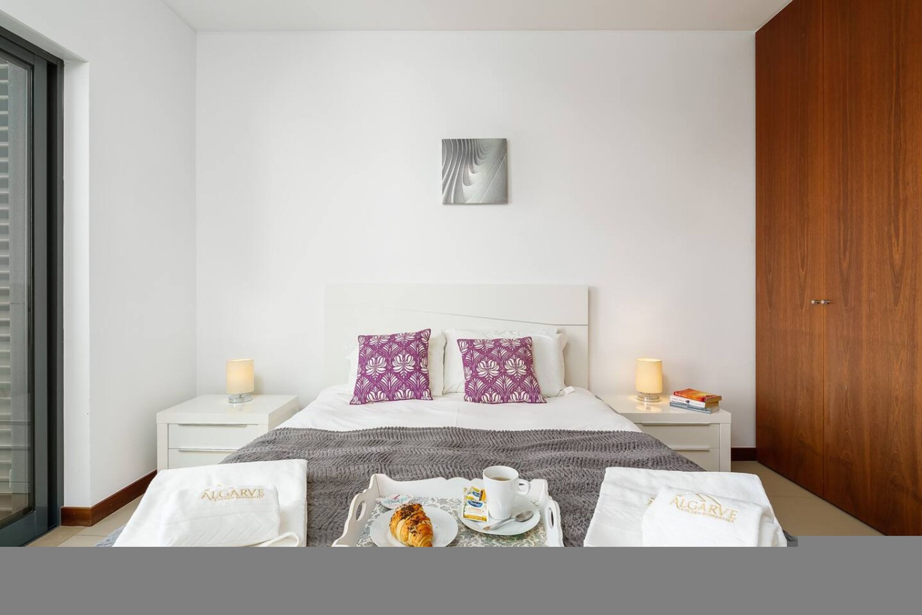 A hotel room with a bed, two nightstands, a wooden door, and a view through a glass door.