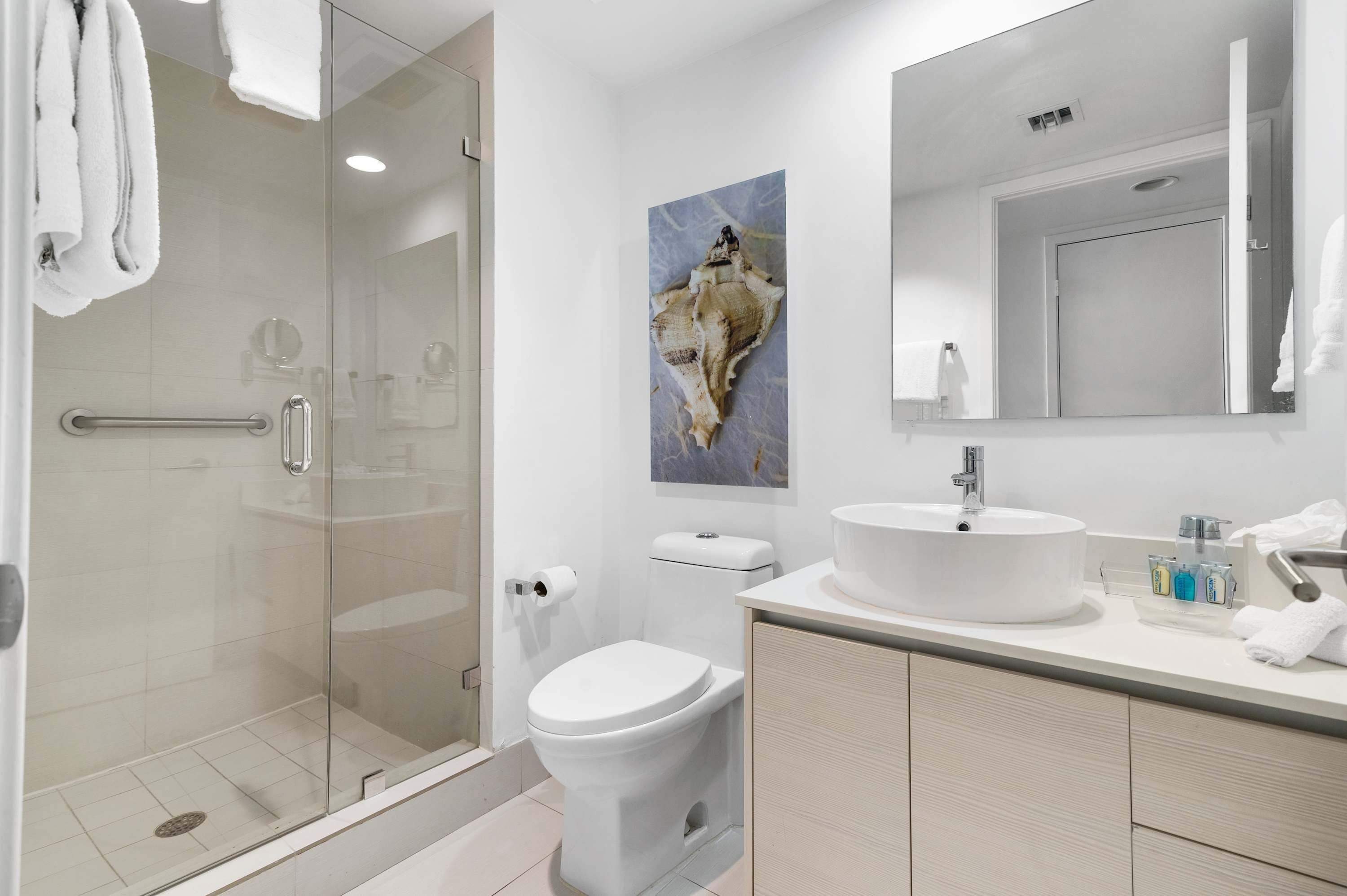 Un baño moderno con cabina de ducha de vidrio, inodoro blanco y lavabo con espejo.