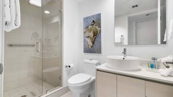 Un baño moderno con cabina de ducha de vidrio, inodoro blanco y lavabo con espejo.