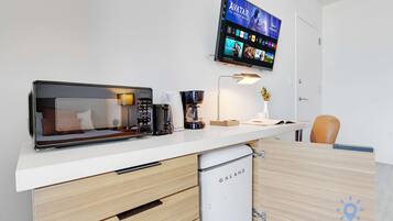 A kitchenette with a microwave, coffee maker, and a small refrigerator. A flat-screen TV mounted on the wall displays a Disney+ interface.