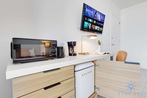Una kitchenette equipada con microondas, cafetera y un refrigerador pequeño. Un televisor de pantalla plana montado en la pared muestra la interfaz de Disney+.