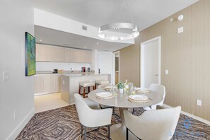 A modern dining area with a round table, white chairs, and a kitchen in the background. - Cozy Apartment With Balcony (Hollywood)