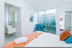 A modern bedroom with a large bed, a bathroom with a mirror and sink, a blue chair, and a sliding glass door leading to a balcony. - Luxury Townhouse in Lagos Old Town Rooftop Terrace (Lagos)
