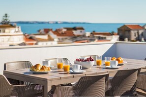 An outdoor dining area with a table set for breakfast, overlooking a coastal town. - Luxury Townhouse in Lagos Old Town Rooftop Terrace (Lagos)