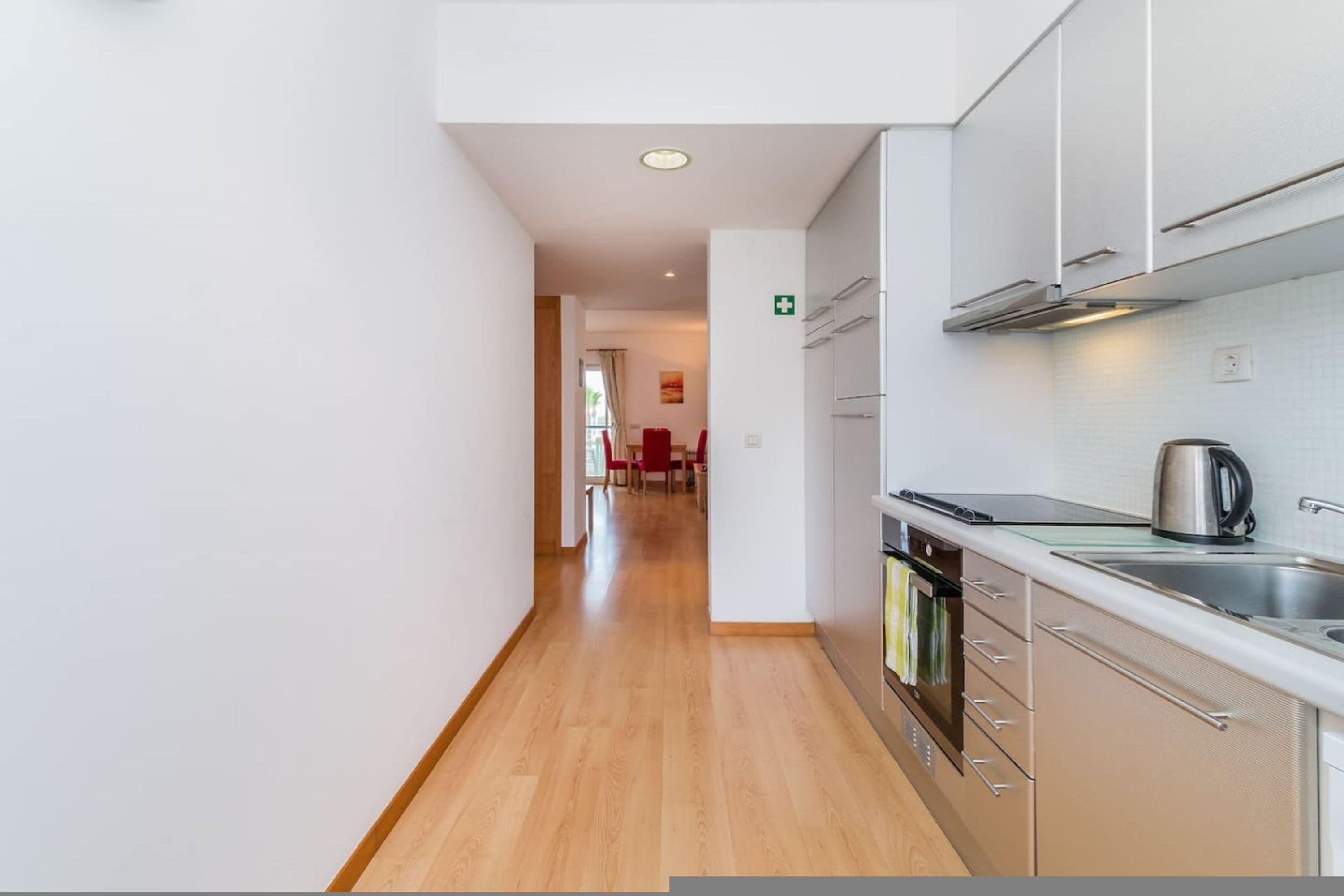 A modern kitchen with stainless steel appliances, a wooden floor, and a view into a dining area.