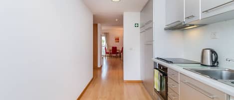 A modern kitchen with stainless steel appliances, a wooden floor, and a view into a dining area.