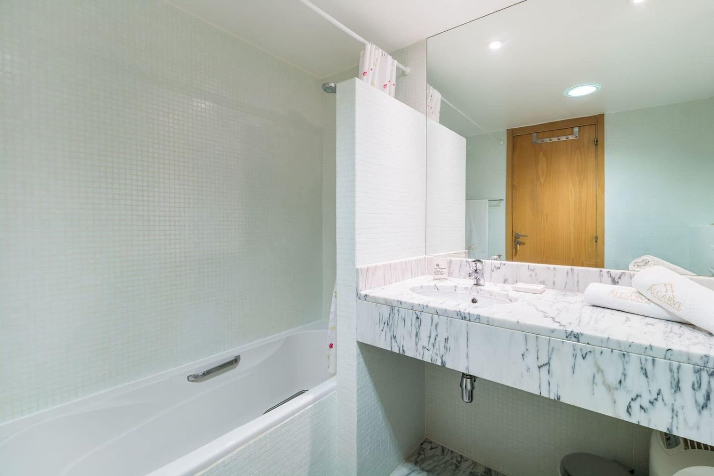 Ein Badezimmer mit einer Badewanne, einem Waschbecken mit Marmorplatte und einem Spiegel über dem Waschbecken.