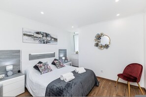 A modern bedroom with a bed, nightstands, a red chair, a wall mirror, and a floral wall decoration. - Torre Verde Sea View Pool AC (Portimão)