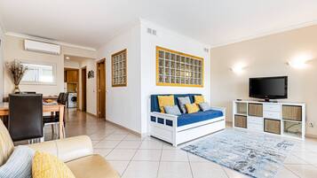 Una sala de estar moderna con un sofá, televisor y una zona de comedor con sillas y una mesa.