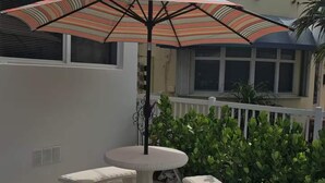 A patio with a table and benches, an umbrella, and a white fence. - Sun Sand Retreat 1BR 1BA (Hollywood)