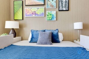 A hotel room with a bed, two bedside lamps, and a wall with framed pictures. - Stylish Apt - Beach View - Resort Access (Hollywood)