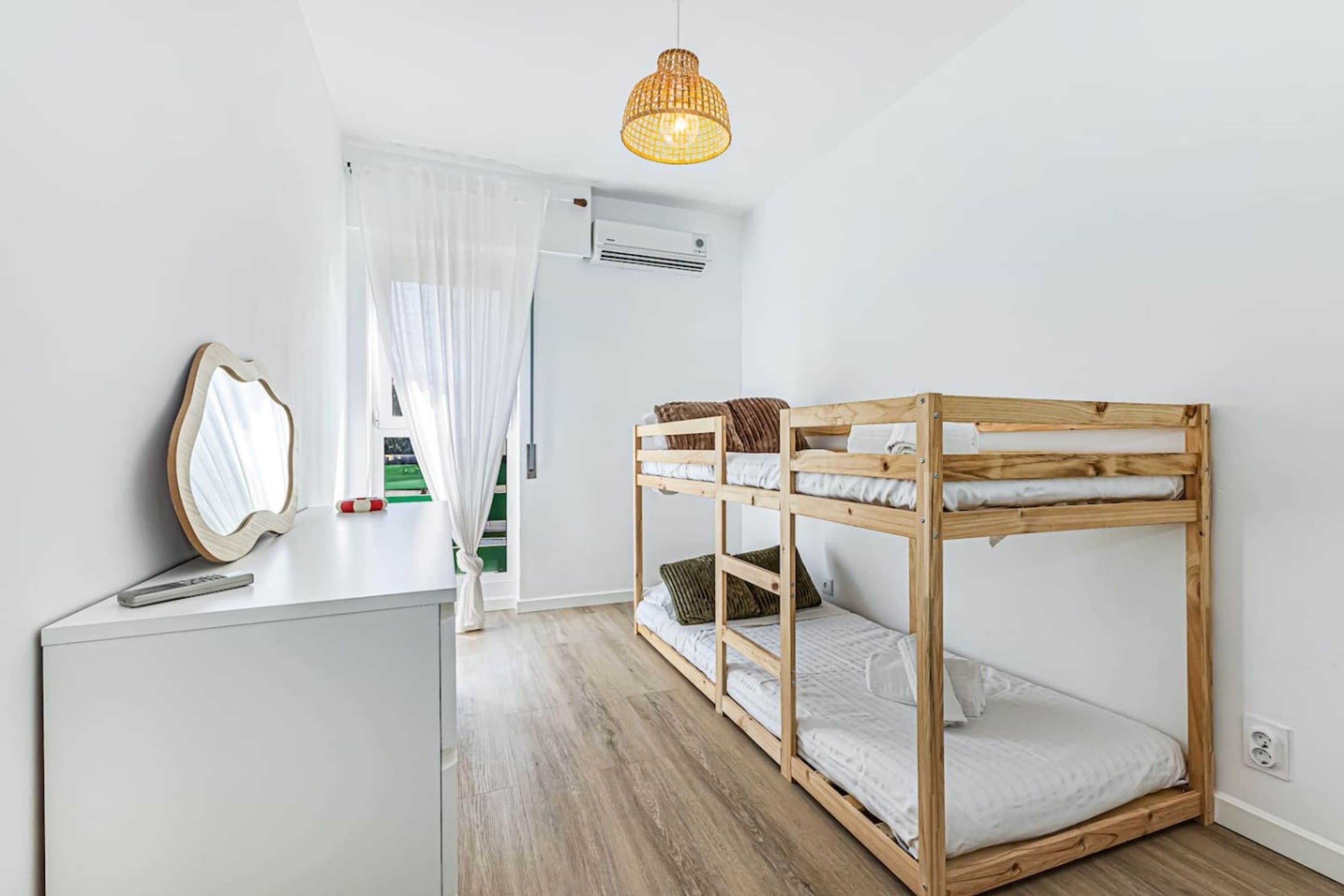 A bunk bed with a wooden frame, a white desk with a mirror, and a hanging light fixture.