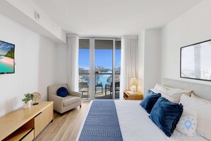 Habitación de hotel con cama, escritorio, silla, balcón y vista panorámica de la ciudad, además de un ventanal amplio.