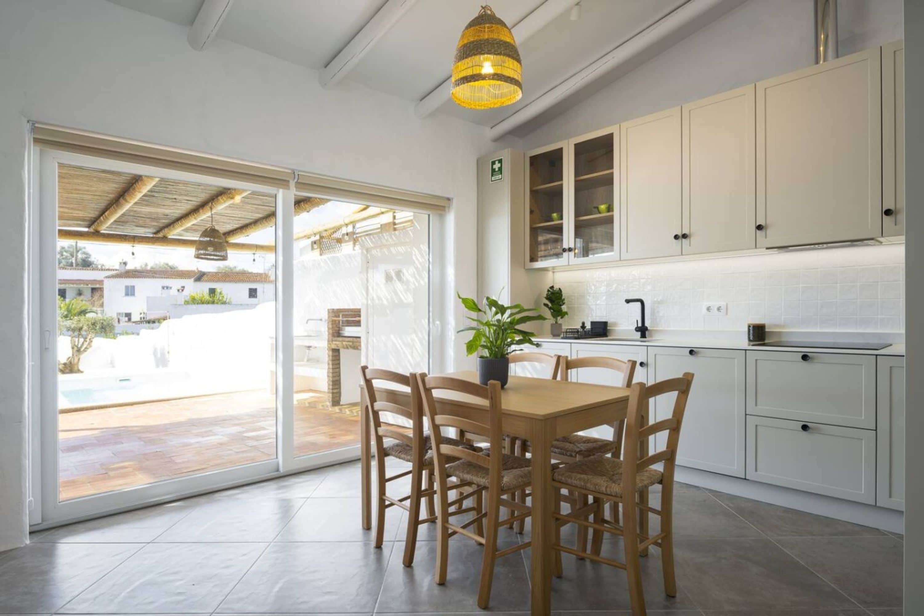 A modern kitchen with white cabinets, a dining table with chairs, and a large window overlooking a pool area.