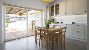 Une cuisine moderne avec des meubles blancs, une table à manger avec des chaises et une grande fenêtre donnant sur un espace piscine.
