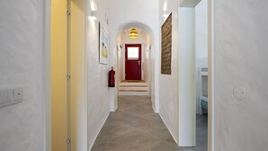 Un pasillo con paredes blancas, una puerta roja al final y un extintor de incendios en la pared.
