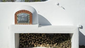 A white building with a brick oven and a pile of firewood.