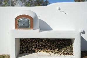 Un edifici blanc amb un forn de rajola i un munt de llenya.