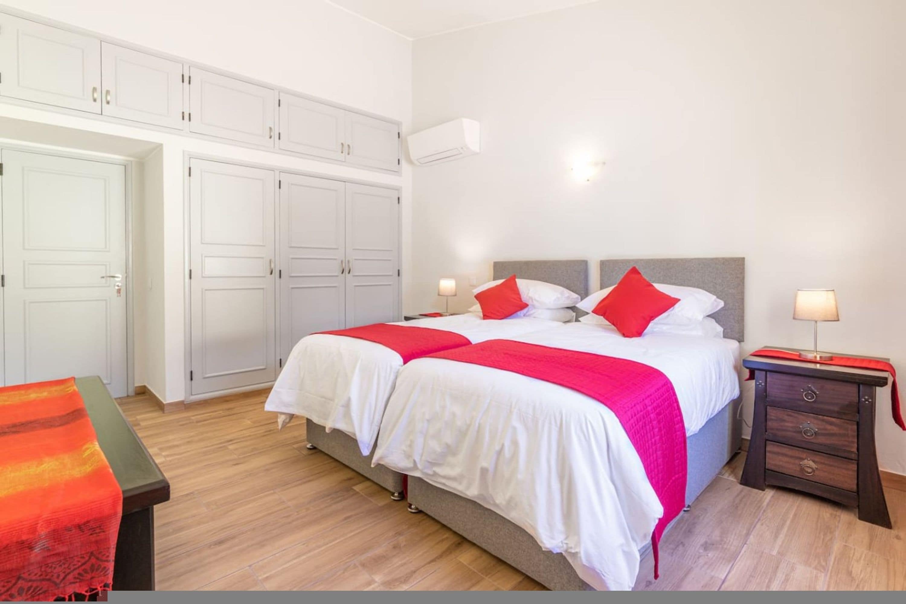 A double bed with white bedding and red pillows, a bedside table with a lamp, and a wardrobe with white doors.