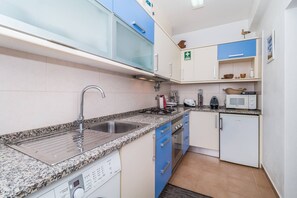Eine kompakte Küche mit einer Granit-Arbeitsplatte, einer Edelstahl-Spüle und einem eingebauten Backofen.