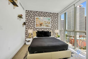 Ein modernes Hotelzimmer mit einem großen Bett, Blick auf die Stadt und einer Wand mit geometrischem Muster.