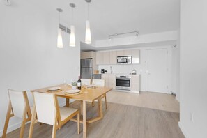 A modern kitchen with stainless steel appliances, a dining area with a wooden table and chairs, and pendant lighting. - Stylish Apartment 2BD 2bth (Hallandale Beach)