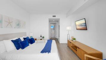 A modern hotel room with a large bed, a wooden bedside table, a TV, and a view of the city through the window.