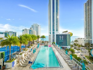 A hotel pool area with a long, rectangular pool, lounge chairs, and palm trees. - Modern 2BD 2BA Resort Luxury Bay Corner Views (Hollywood)