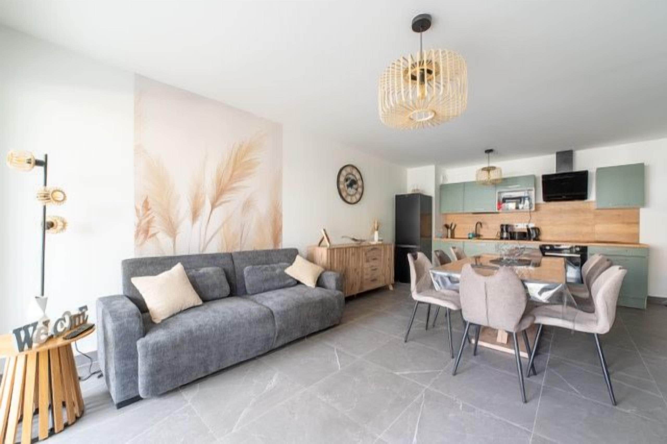 A modern living room with a grey sofa, dining table, and chairs, a kitchen area with green cabinets, and a large wall art piece.