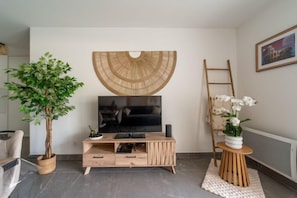 Ein Wohnzimmer mit Fernseher, einer Holz-Unterhaltungsecke, einer Topfpflanze, einer Leiter und einer Vase mit Blumen.