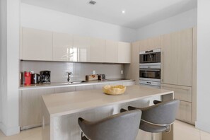 A modern kitchen with a central island, two chairs, a coffee maker, a toaster, and a microwave. - 2BR Ocean View Balcony Pool (Hollywood)