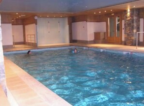 An indoor swimming pool with a tiled floor, a person swimming, and a stone wall. - Apartment with 2 large balconies, mountain view (Cohennoz)