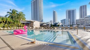 A swimming pool with lounge chairs and a pink flamingo float, surrounded by palm trees and high-rise buildings. - Spectacular Apartment With Amazing Pool (Hallandale Beach)