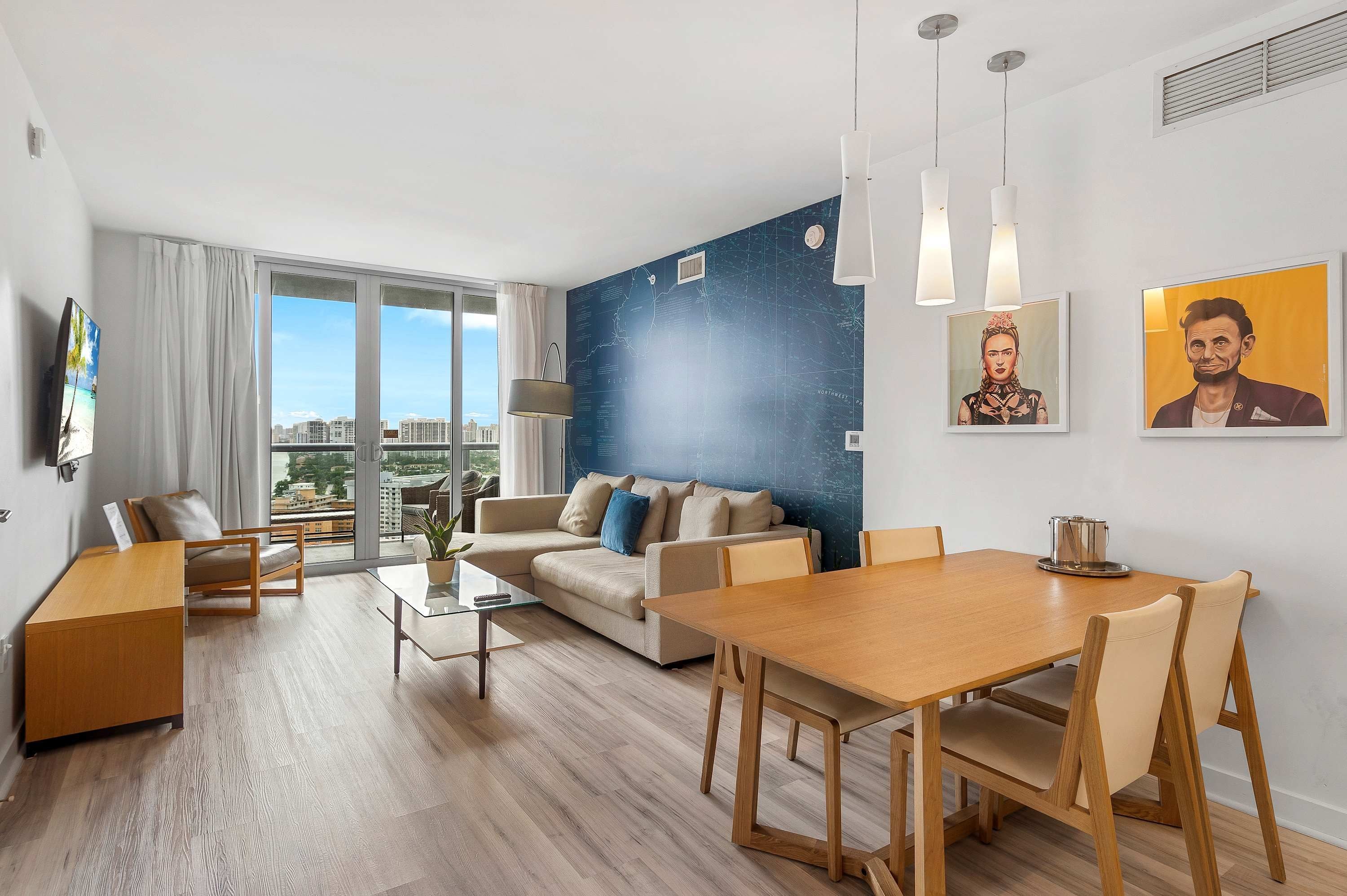 Una sala de estar moderna con un sofá, una mesa de comedor y sillas. Se aprecia un amplio ventanal con vistas a edificios.