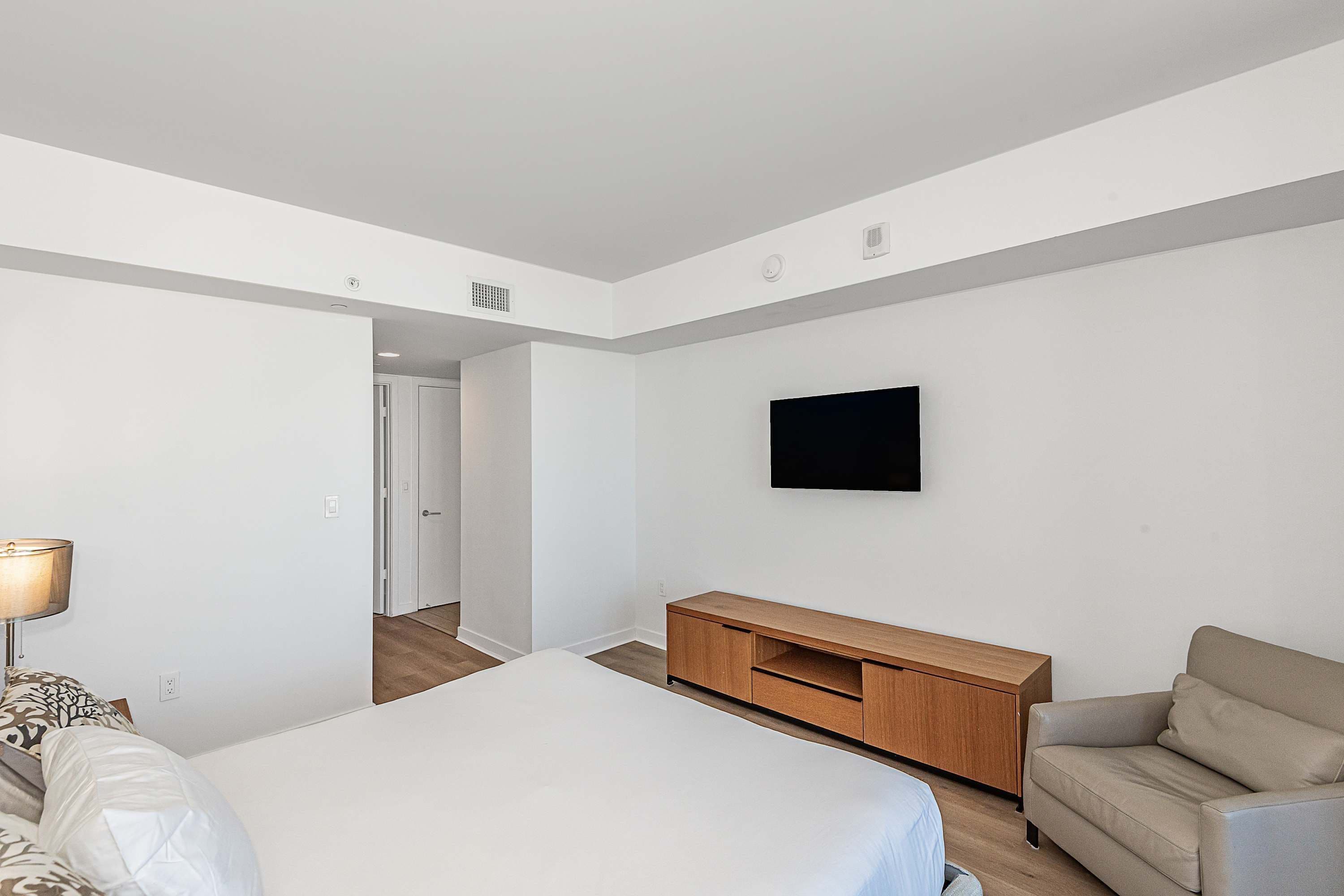 Quarto de hotel com cama, televisão presa na parede, armário de madeira e sofá.