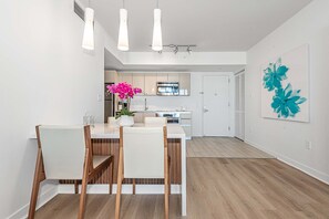 Una cocina moderna con armarios blancos, horno de acero inoxidable y comedor con mesa y sillas de madera.
