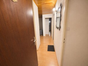A hallway with wooden flooring, a door on the left, and a mirror on the right. - Le Cygne - 6-guest balcony apartment (Les Deux Alpes)