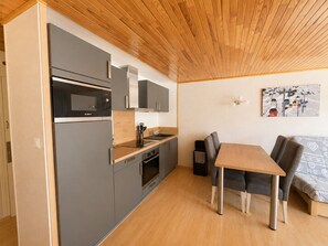 A compact kitchen with modern appliances, a dining area with a table and chairs, and a wall-mounted light fixture. - Le Cygne - 6-guest balcony apartment (Les Deux Alpes)